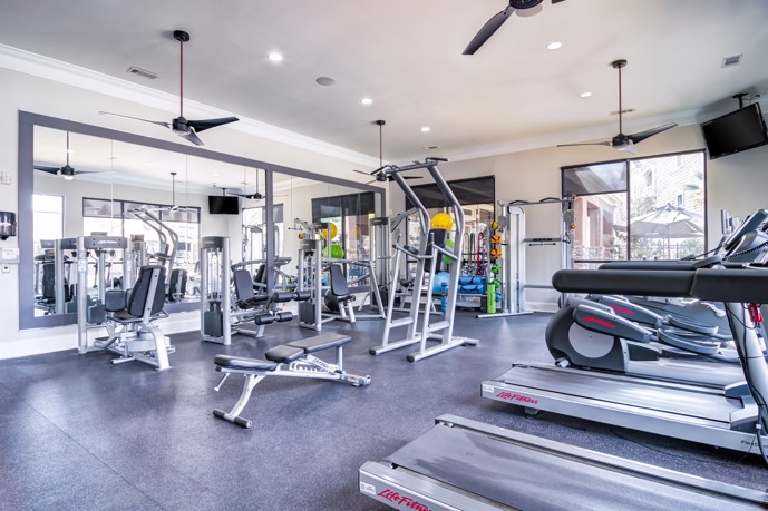 A fitness center equipped with exercise equipment, a spacious wall mirror, and ceiling fans to keep you cool during your workouts at Waterstone at Big Creek in Alpharetta, GA.
