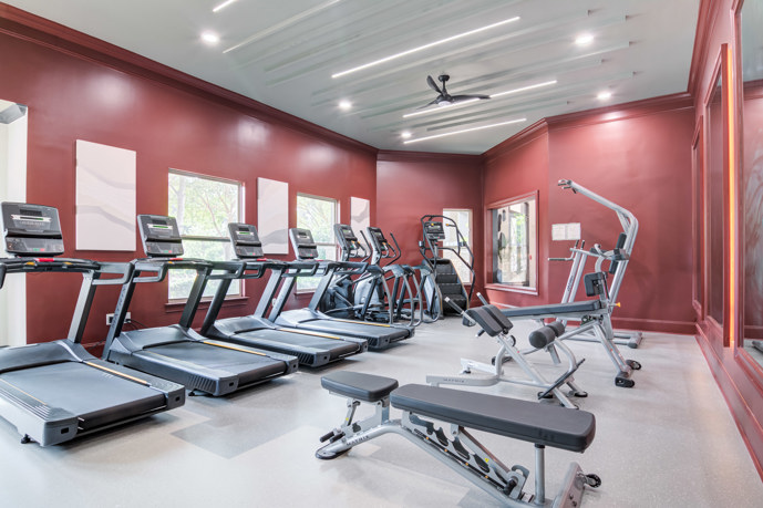 A fitness center equipped with exercise equipment, a spacious wall mirror, and ceiling fans to keep you cool during your workouts at Waterstone at Big Creek in Alpharetta, GA.