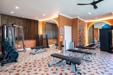 The fitness center at The Pointe at Vista Ridge boasts a variety of gym equipment and vibrant, colorful flooring throughout, creating an energizing and inviting atmosphere for residents to work out.