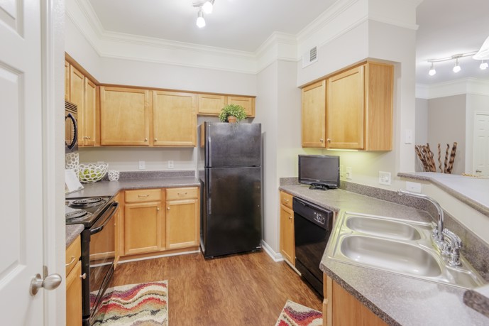 Classic apartment kitchen with hardwood floors, light wooden cabinets, and black appliances