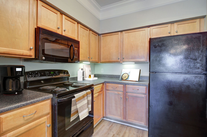Classic apartment kitchen with hardwood floors, light wooden cabinets, and black appliances