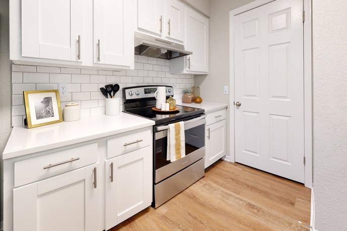 The Landings of Brentwood offers a cozy apartment kitchen equipped with white shaker-style cabinets, wood-style flooring, and a door for added privacy.