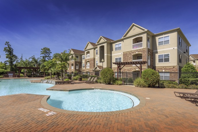 Outdoor swimming with brick patio, landscaping, and Carrington at Champion Forest apartments behind it