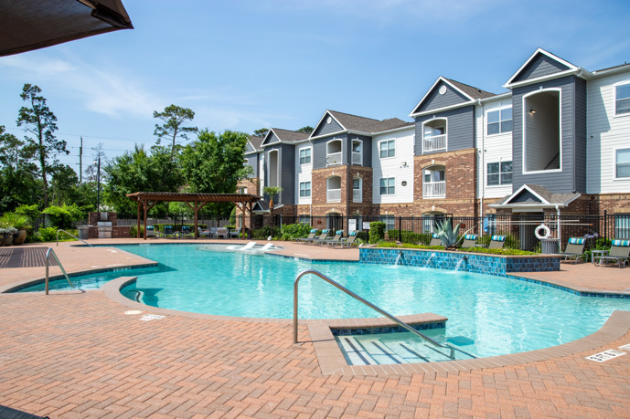 Outdoor swimming with brick patio, landscaping, and Carrington at Champion Forest apartments behind it