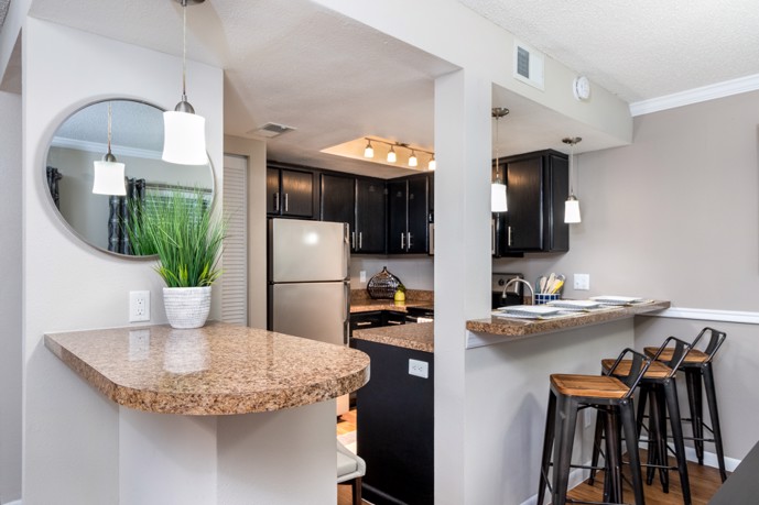 A kitchen is adorned with track and pendant lighting, a breakfast bar, and hardwood-style flooring, complemented by a built-in side table along one wall.