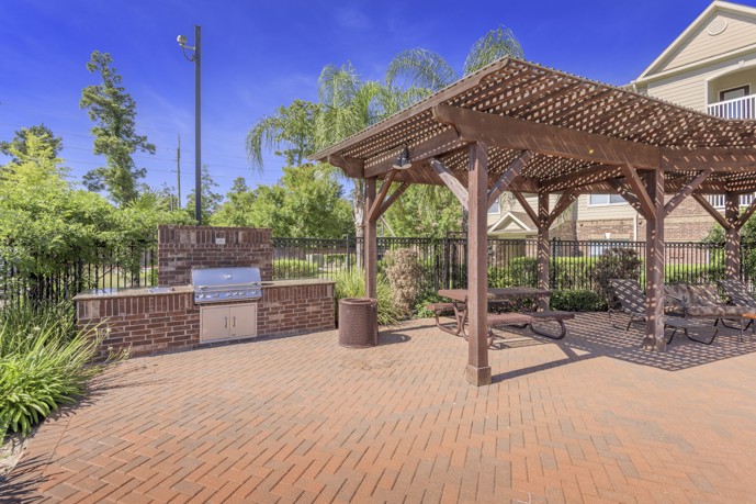 Outdoor apartment community grilling area with brick patio, gas grill, and a wooden veranda with seating under it
