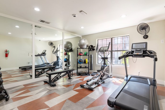 A well-equipped fitness center at The Augusta apartments, offering residents a variety of gym equipment options, complemented by a large mirror and window to create an energizing workout environment.