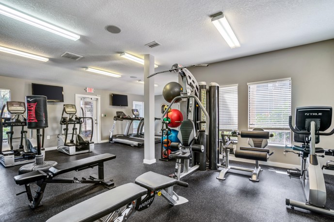 A fitness center, equipped with cardio and weight machines, ample windows for natural light, and TVs for entertainment.