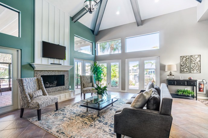  A clubhouse featuring cozy seating around a fireplace lounge, boasting vaulted ceilings, tiled floors, and expansive windows.