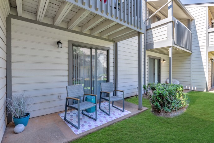 An exterior patio adorned with two chairs, nestled amidst lush grass, providing a tranquil outdoor retreat for residents to enjoy at The Invitational apartments in Oklahoma City, Oklahoma.