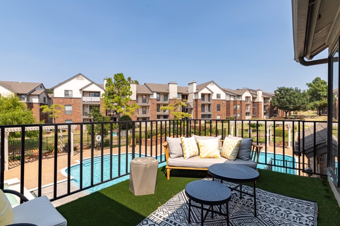 A sizable balcony boasting lounge seating arrangements, offering picturesque views overlooking the shimmering pool at The Augusta apartments in Oklahoma City, Oklahoma.
