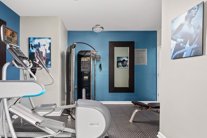 Small community fitness center with grey and blue walls and a few pieces of exercise equipment at Arbors River Oaks apartments