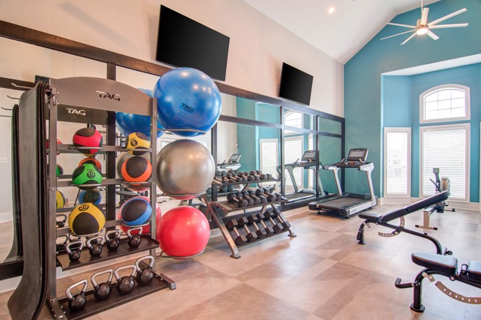 A spacious fitness center filled with a variety of gym equipment, each offering different workout options, accompanied by multiple TVs and illuminated by abundant natural light streaming in through large windows at Waterford Landing apartments.