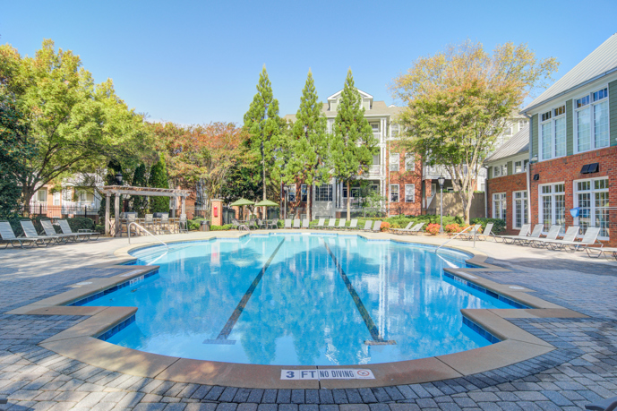 The enticing resort-style pool surrounded by loungers, situated just outside the clubhouse at The Residences on McGinnis Ferry, offering residents a luxurious outdoor space for relaxation and leisure.