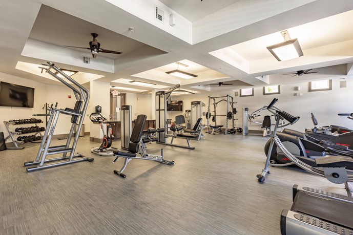Indoor fitness center with various exercise equipment and weights, plank flooring, and ceiling lights and fans