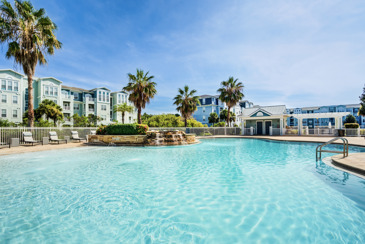 Pool area at The Enclave in Riverview, FL, featuring a spacious swimming pool surrounded by lounge chairs, umbrellas, and lush landscaping.