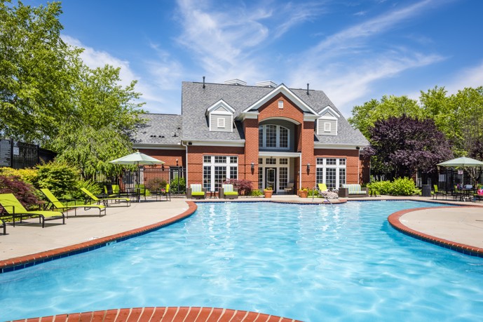 Large curved outdoor swimming pool with red brick edging and cement ground and large brick pool house in the background at Columns on Wetherington apartments in Florence, KY