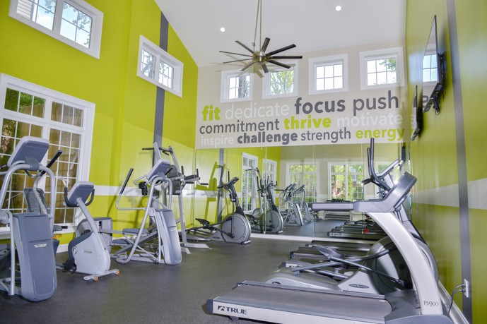 The spacious fitness center at The Residences on McGinnis Ferry, characterized by vibrant green walls, lofty ceilings, and expansive windows, creating an energizing atmosphere for residents' workouts.
