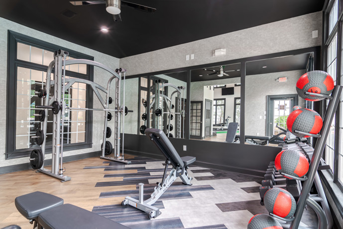 The spacious fitness center at The Residences on McGinnis Ferry, characterized by vibrant green walls, lofty ceilings, and expansive windows, creating an energizing atmosphere for residents' workouts.