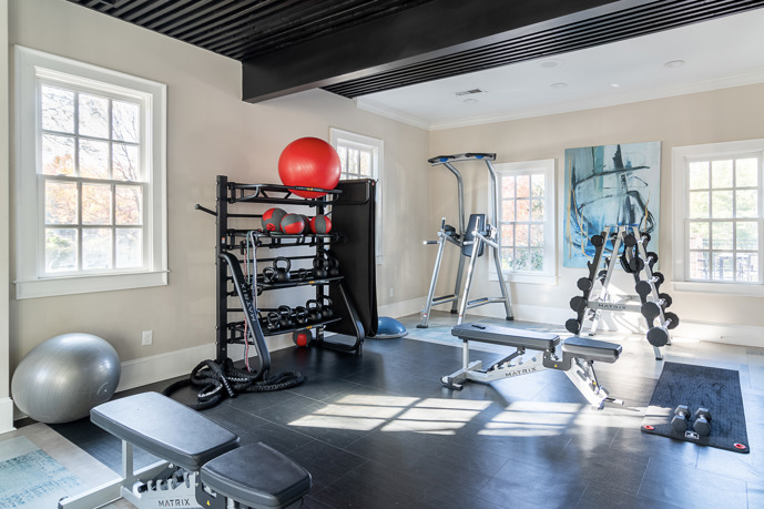 The spacious fitness center at The Residences on McGinnis Ferry, characterized by vibrant green walls, lofty ceilings, and expansive windows, creating an energizing atmosphere for residents' workouts.