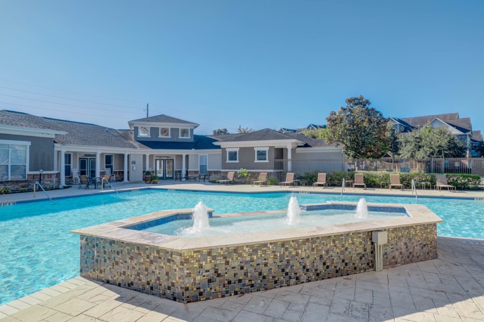 Outdoor swimming pool with a jetted hot tub in the foreground a slate patio surrounding it, and Houston, TX apartments behind it