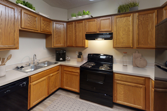 A spacious U-shaped kitchen boasting hardwood-style flooring, a breakfast bar, and wooden cabinets, seamlessly connected to a cozy carpeted living room.