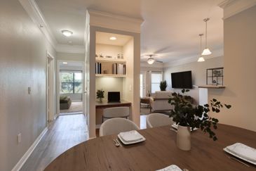 Open-concept empty apartment with vinyl plank flooring, narrow built-in shelving dividing the room in half, and pendant lighting