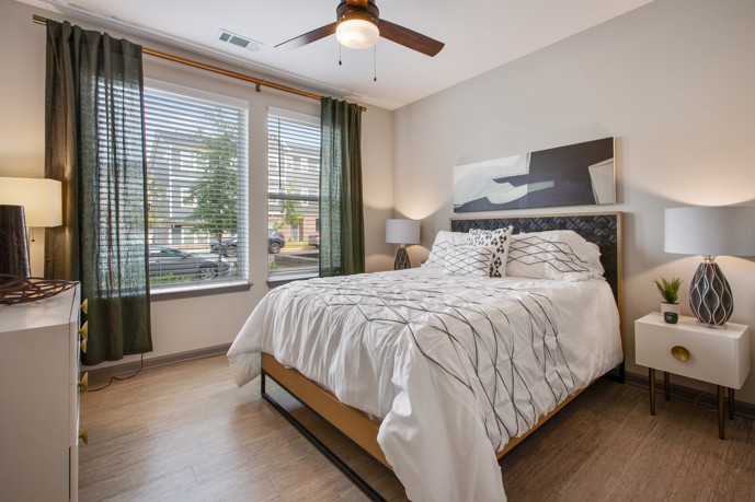 At the Vesta City Park apartments, you can find a stylish bedroom featuring a generously-sized window, a comfortable queen bed, a spacious armoire, and two convenient bedside tables.