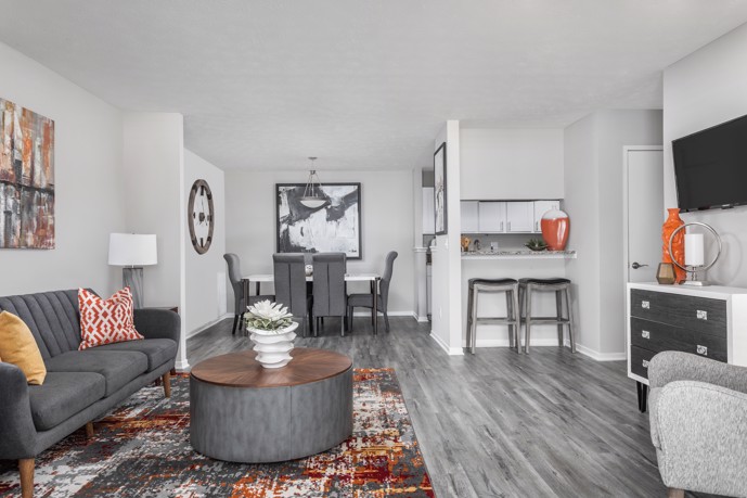 The Pointe at Canyon Ridge, apartment with an open floor plan featuring a sleek grey 3-seater couch, a designated dining area, and a modern kitchen.