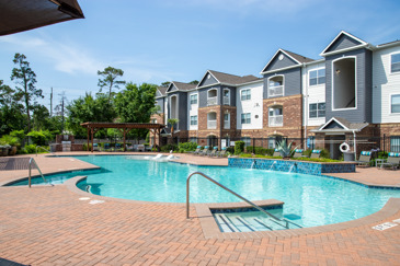 Large brick patio with a resort-style swimming pool surrounded by trees and apartment buildings