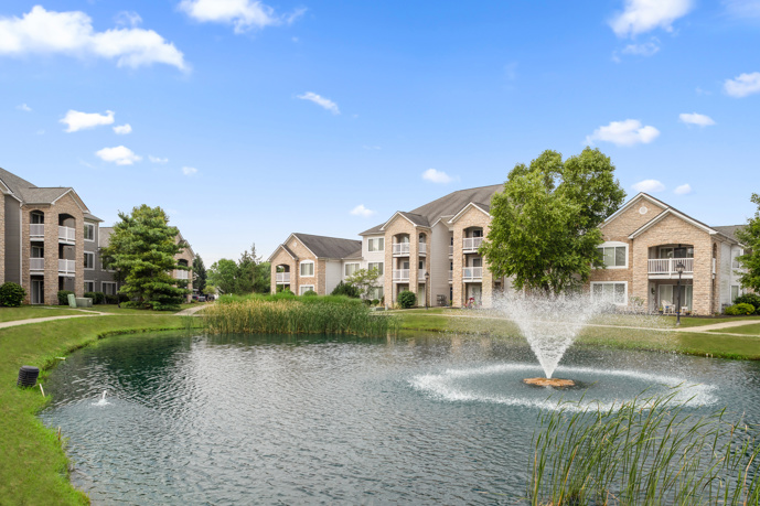 Long view of  an apartment community clubhouse with two blue arm chairs in the foreground, a kitchenette to the left, and fireplace with more seating in the distance