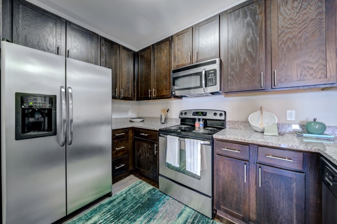 Classic apartment kitchen with dark wood cabinets, granite countertops, and stainless steel appliances