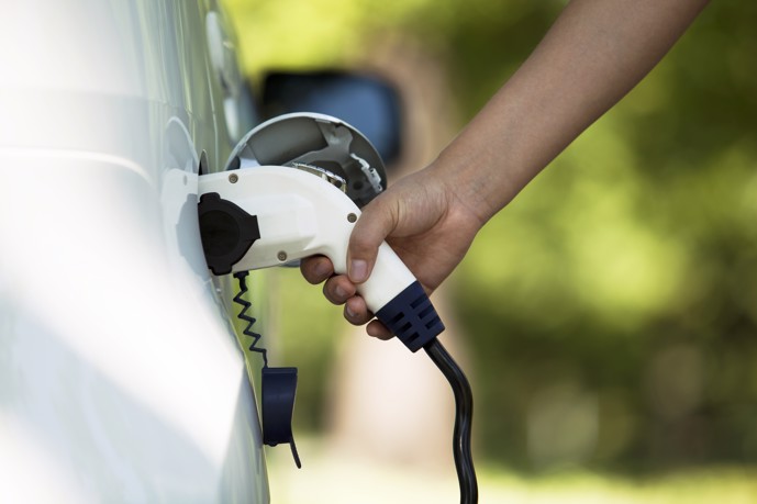 Power up your electric vehicle at Garrison Station's state-of-the-art charging station, as demonstrated by a hand plugging in a car for charging.