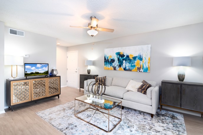 A cozy living room adorned with a plush three-seater couch, an elegant armoire, and a cooling ceiling fan, creating a comfortable and inviting space for residents to unwind at Vantage on Hillsborough in Tampa, Florida.