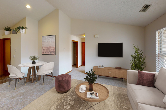 A comfortable carpeted living room, offering seamless access to the kitchen and situated near a staircase leading to a second level.