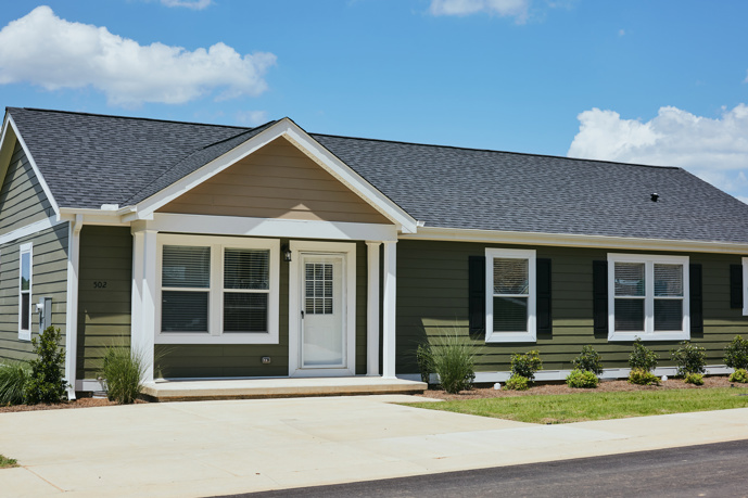A queen bed in a carpeted bedroom with two sizable windows and a prominent owl painting at Virtuoso Apartments.