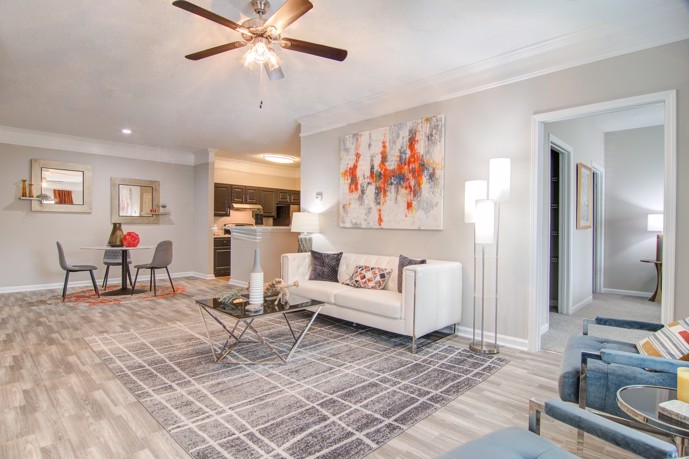 A generously sized living room featuring light wood-style flooring, an adjoining dining space centered around a round table, and a well-appointed kitchen with a sleek quartz countertop at Waterford Landing.