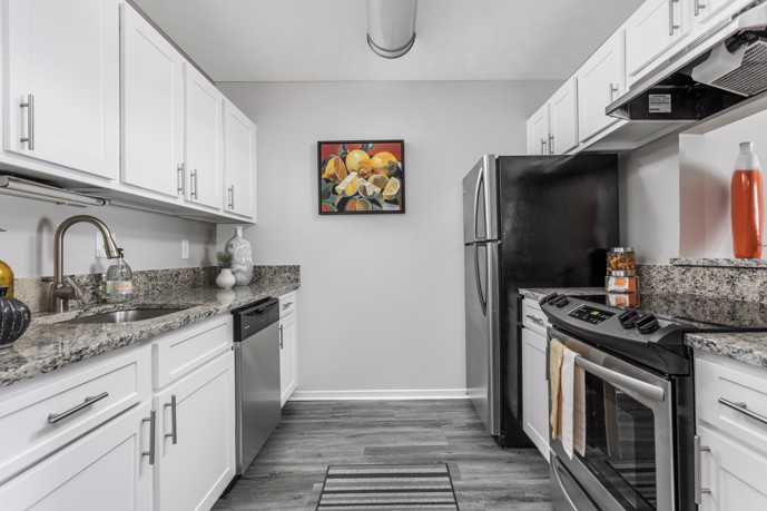 Pointe at Canyon Ridge features a modern galley kitchen equipped with white cabinets, grey wood-style flooring, and stainless steel appliances.