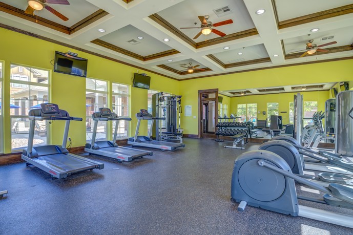A state-of-the-art gym at The Shores in Oklahoma City, Oklahoma, offering a multitude of exercise options with various gym equipment, accompanied by TVs for entertainment and large windows flooding the space with natural light.