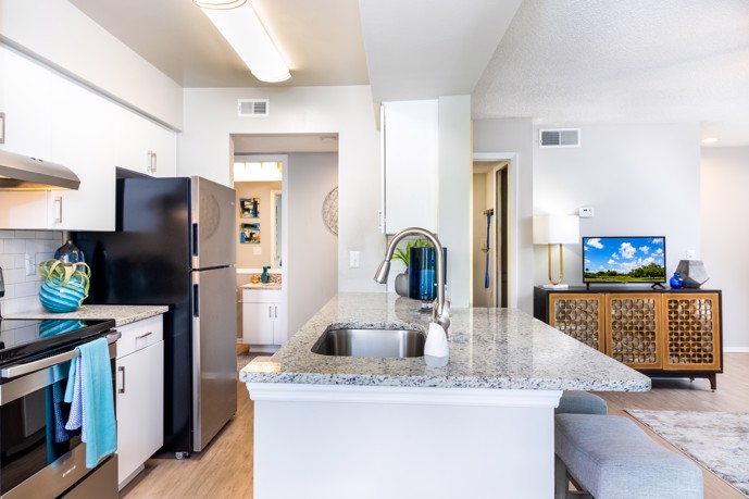 At Vantage on Hillsborough in Tampa, Florida, a sleek modern kitchen boasting granite countertops, gleaming stainless steel appliances, and seamlessly integrated living room space, providing residents with a contemporary and functional culinary gathering area.
