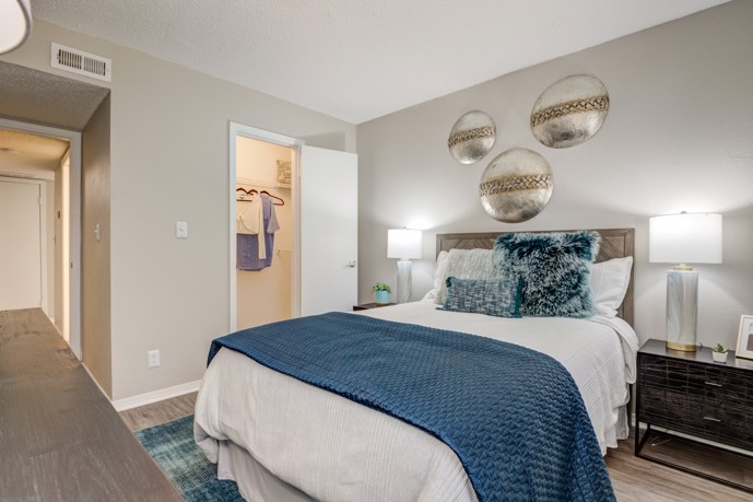 A comfortable bedroom at The Invitational, furnished with a queen bed, soft carpeting underfoot, and a compact closet, providing residents with a cozy retreat for rest and relaxation.