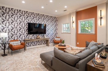 The clubhouse TV room at The Pointe at Vista Ridge showcases colorful wallpaper, a comfortable couch, and large windows, creating a cozy and inviting space for residents to relax and unwind.