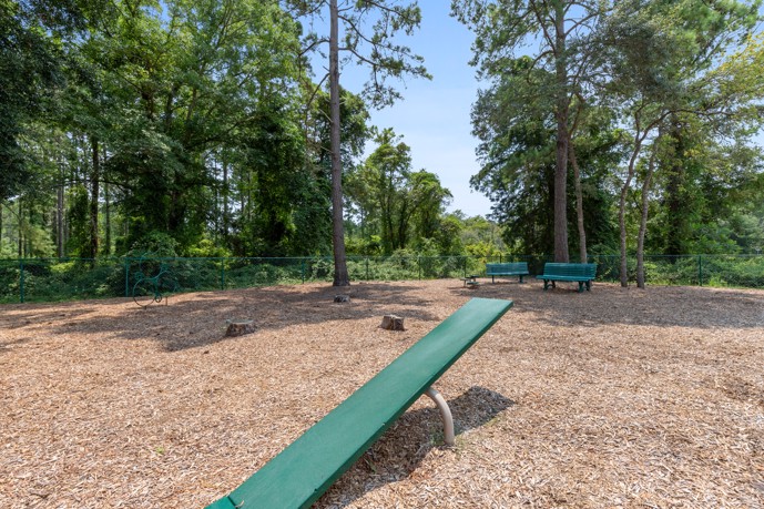 A fenced dog park nestled within a secluded wooded area at The Tides of Calabash, offering a tranquil and safe environment for furry companions to play and socialize.