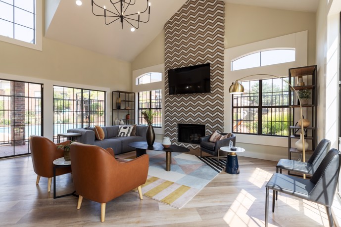 A grand lounge area within the clubhouse at The Augusta apartments, characterized by lofty ceilings, expansive windows flooding the space with natural light, and an array of comfortable lounge chairs for residents to relax and socialize.