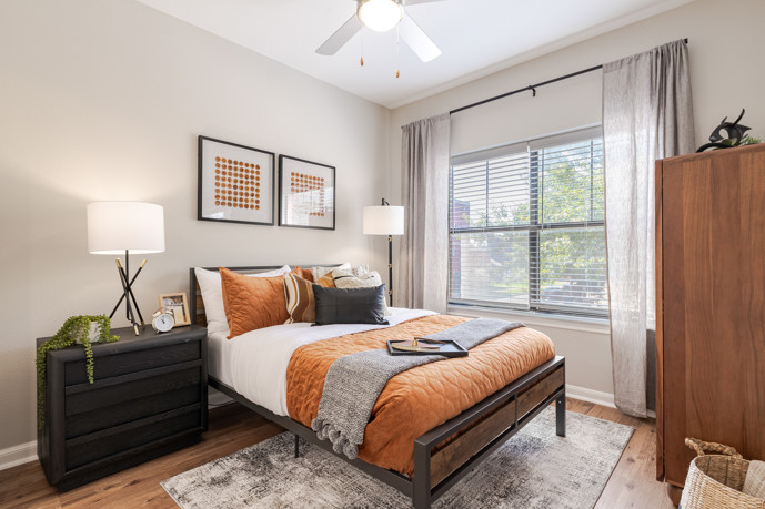 Serene grey apartment bedroom furnished with a bed, nightstands with table lamps, wall art, and an open closet door