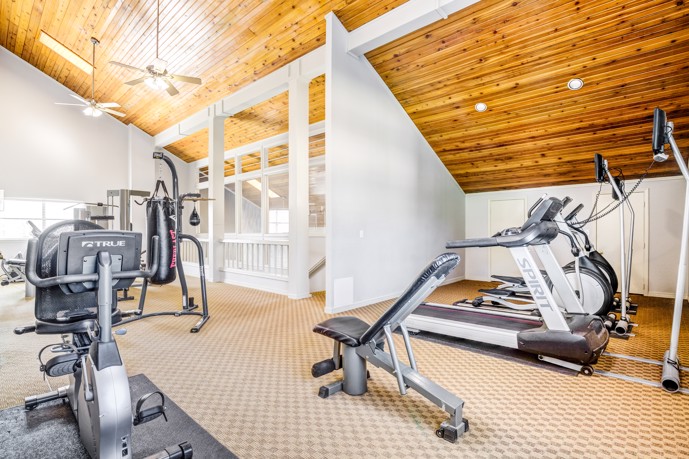 The carpeted fitness center at Windrush apartments in Edmond, OK, featuring a wide range of gym equipment options.