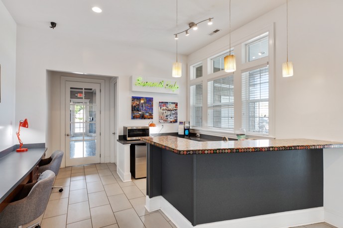 Clubhouse showcasing a community kitchen, a built-in desk with two chairs, abundant natural light pouring in through its large windows, and stylish tile flooring.