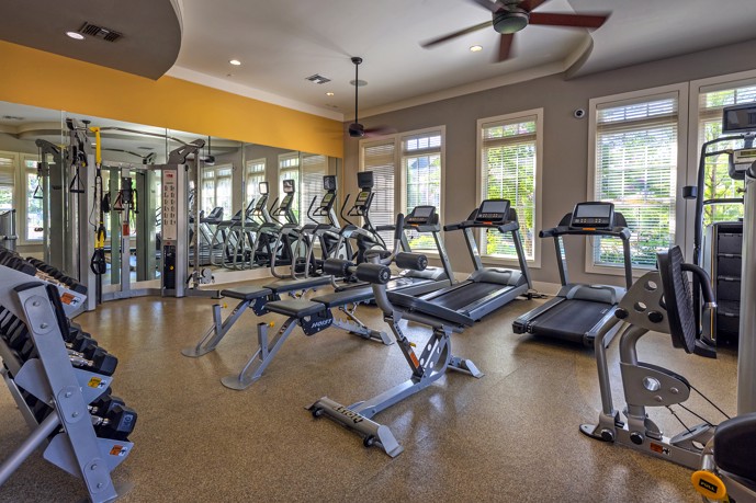 Fitness center featuring weight and cardio equipment, ample windows, mirrors, and a ceiling fan.