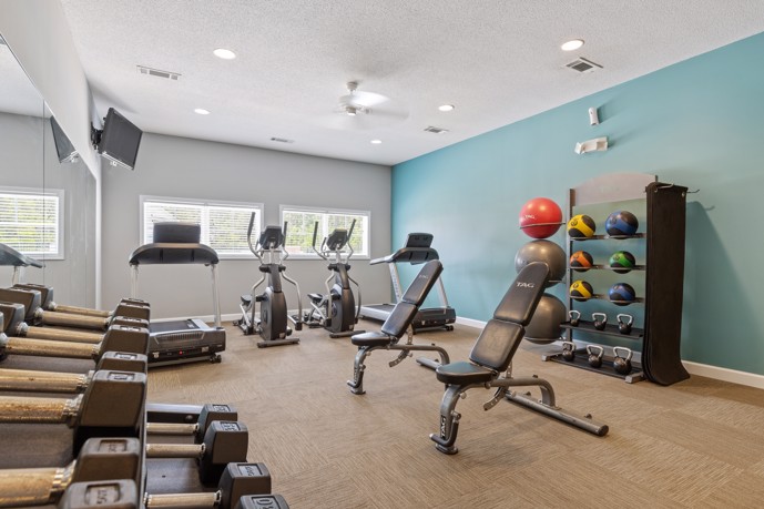 The carpeted fitness center at The Tides of Calabash in Sunset Beach, North Carolina, featuring a variety of exercise equipment, providing residents with a convenient and comfortable space for maintaining their health and wellness.