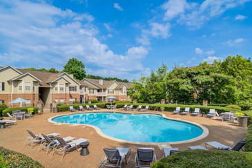 A resort-style pool with lounge chairs and table surrounding it and in the distance large trees at Waterford Landing. 